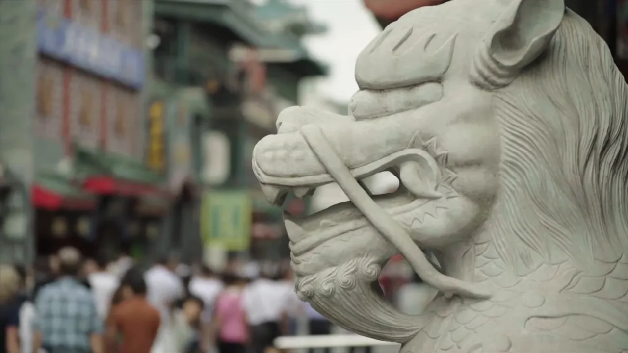 Close-up of a stone statue of an elderly person in a busy street in China