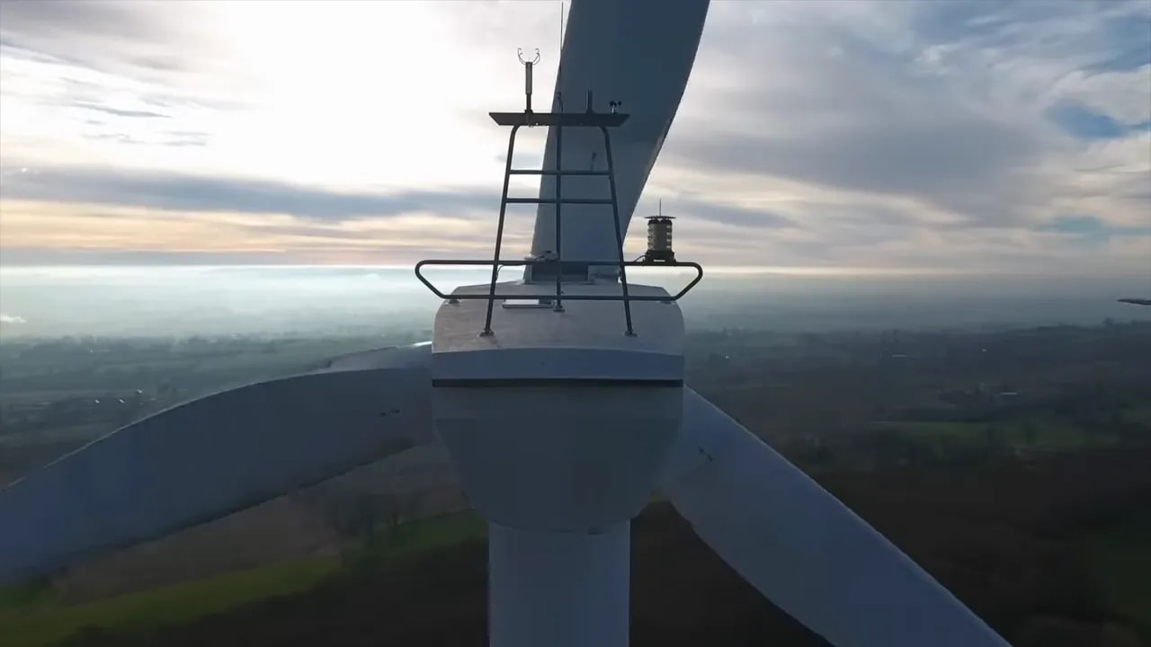 Close-up view of an offshore wind turbine nacelle and blades above a landscape at dusk