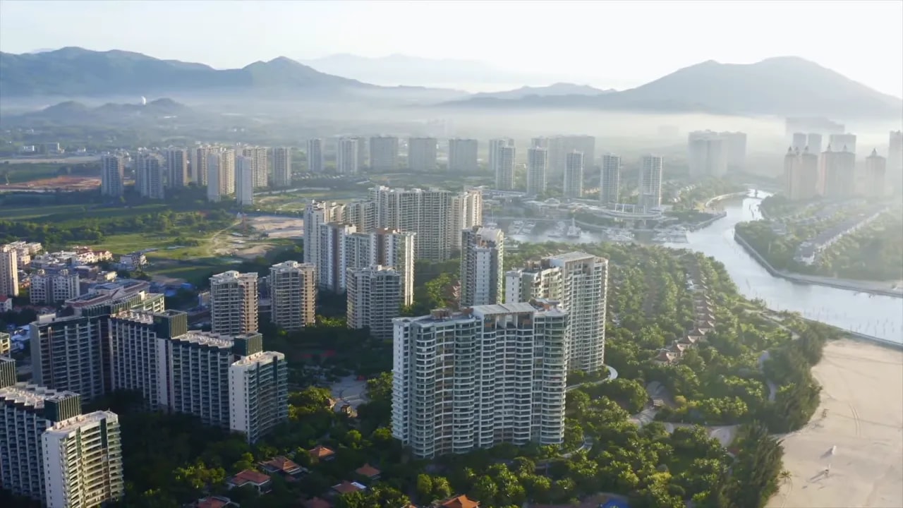 Clear aerial view of high-rise buildings and a river with a bridge, representing Hainan development