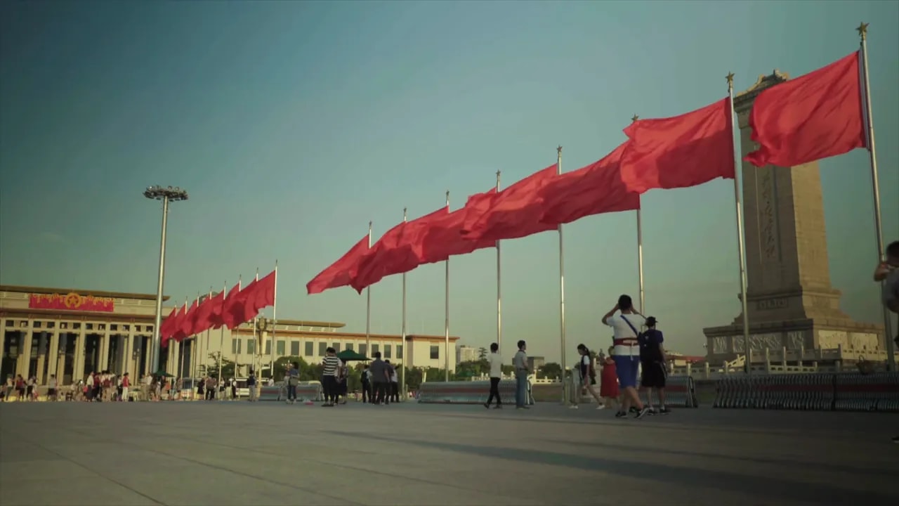 Wide view of a Chinese plaza with multiple red flags and people walking